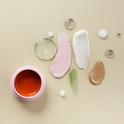 Different cosmetic smears with concealer, lipstick, mask, face cream, serum. On a light beige background. view from above.